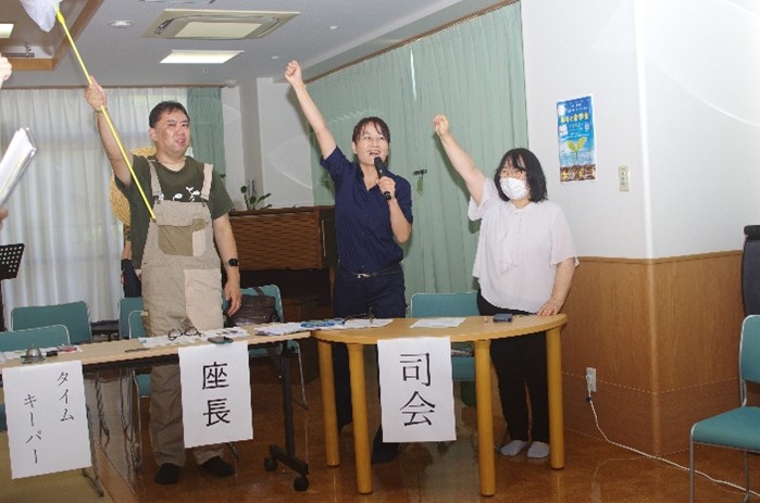 腕をつき挙げる司会と座長